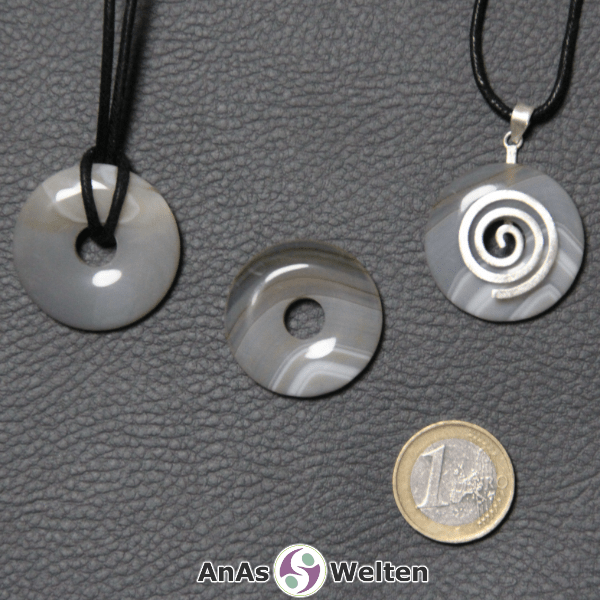 Drei Achat Donuts nebeneinander. Einer an einem Baumwollband, ein anderer an einem Donut-Halter mit Baumwollband.