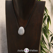 Das Bild zeigt einen gebohrten Achat Trommelstein an einem Baumwollband. Der gebohrte Achat Trommelstein ist grau mit blau-grauen und weißen Streifen.