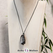 Ein Achat Geode Rohstein als Kette an einem schwarzen gewachsten Baumwollband um eine helle Büste.