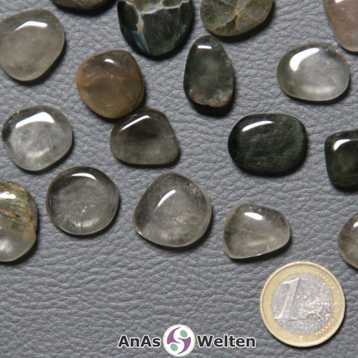 Das Produktbild zeigt mehrere Beispiele für einen Aktinolith Trommelstein. Man sieht hier gut die unterschiedlichen Farben, die der Stein haben kann. Mal ist er durchsichtig, mit einer schwachen gelb-bräunlichen Trübung und Musterung, mal ist er braun, mal dunkelgrün und mal gräulich. Auch kann man seine unregelmäßige Musterung gut erkennen.