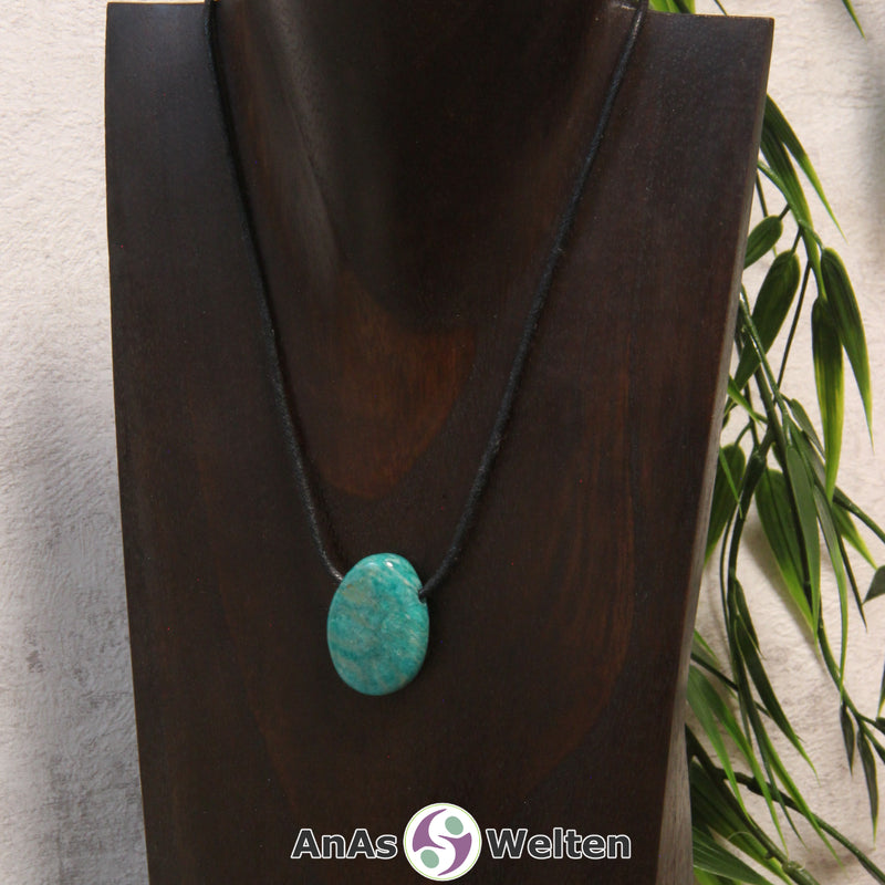 Ein blau-grüner Amazonit gebohrter Trommelstein an einem schwarzen Baumwollband, der um eine dunkle Büste gehängt wurde.