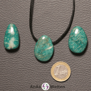 Drei blau-grüne Amazonit gebohrte Trommelsteine nebeneinander. Einer befindet sich an einem schwarzen gewachsten Baumwollband.