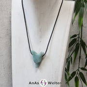 Ein Amazonit Wolf Anhänger an einem schwarzen Baumwollband, der um eine dunkle Büste gehängt wurde.