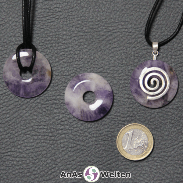 Drei Amethyst Donuts nebeneinander. Einer an einem Baumwollband, ein anderer an einem Donut-Halter mit Baumwollband.