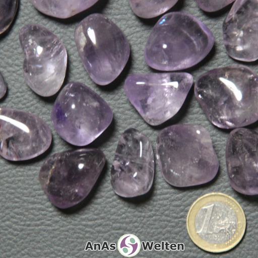 Das Bild zeigt den Amethyst Trommelstein anhand mehrerer Beispiele. Die Edelsteine variieren dabei in ihren Lilatönen, sind aber alle halbdurchsichtig und haben gelegentlich kleine Einschlüsse und Risse im Inneren.