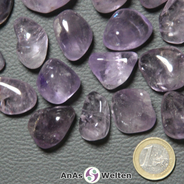 Das Bild zeigt den Amethyst Trommelstein anhand mehrerer Beispiele. Die Edelsteine variieren dabei in ihren Lilatönen, sind aber alle halbdurchsichtig und haben gelegentlich kleine Einschlüsse und Risse im Inneren.