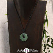 Das Bild zeigt einen Aventurin Donut an einem Baumwollband. Der Edelsteindonut hat einen sanften Grünton und weist keine sichtbaren Einschlüsse oder Risse im Inneren auf.