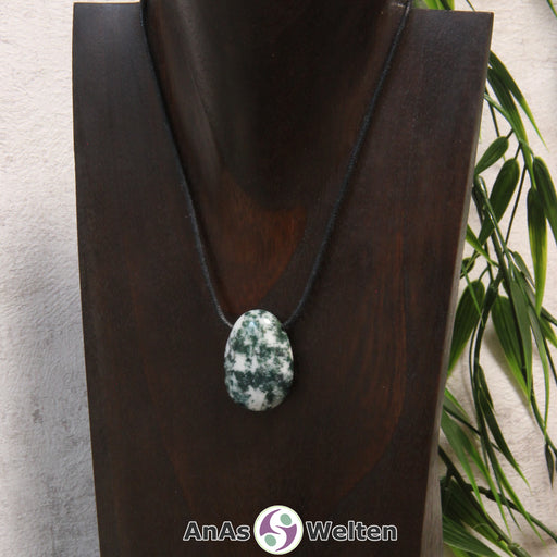 Ein gebohrter Baumachat Trommelstein an einem Baumwollband. Der Edelstein hat eine fleckige dunkelgrüne und weiße Farbe.
