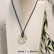 Ein Bergkristall Donut als Kette an einem schwarzen gewachsten Baumwollband um eine helle Büste.