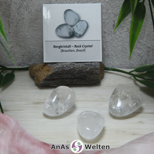 Das Bild zeigt drei Beispiele für den Bergkristall Trommelstein mit Sticker. Der Bergkristall ist ein farbloser bis weißer Edelstein, in dessen Inneren man deutlich die eingeschlossenen Risse erkennen kann. Im Hintergrund ist der Sticker zu sehen.