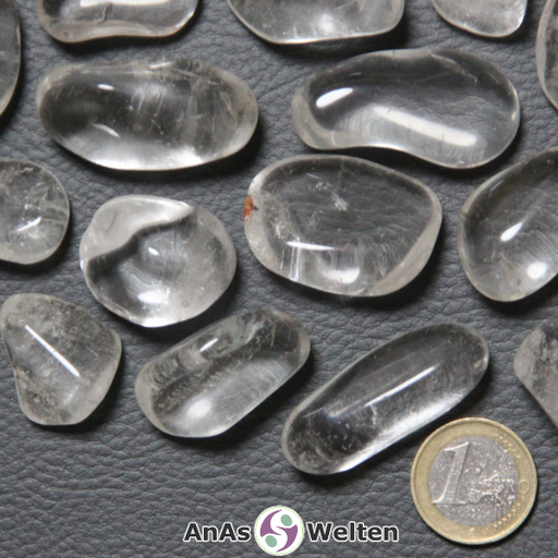 Das Produktbild zeigt mehrere Beispiele für einen Bergkristall Trommelstein. Die Edelsteine sind durchsichtig und sehr klar, weisen aber gelegentliche Einschlüsse und Risse im Inneren auf.