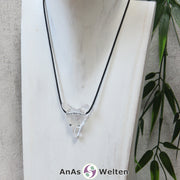 Ein Bergkristall Wolf Anhänger an einem schwarzen Baumwollband, der um eine dunkle Büste gehängt wurde.