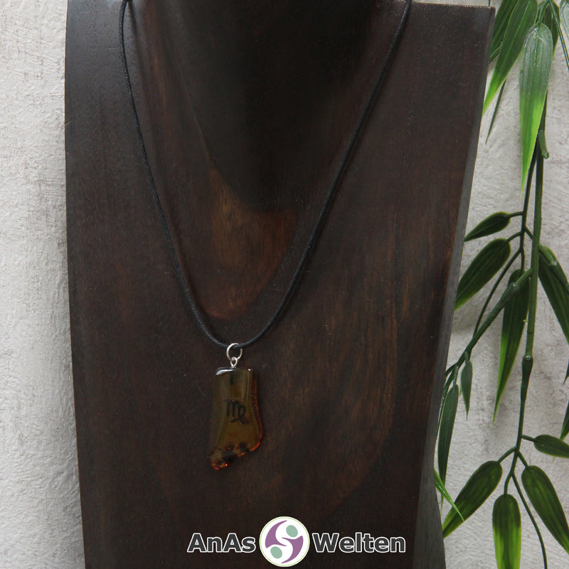 Ein Bernstein Anhänger Jungfrau an einem Baumwollband als Kette um eine dunkle Büste.