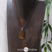 Ein Bernstein Anhänger Löwe an einem Baumwollband als Kette um eine dunkle Büste.