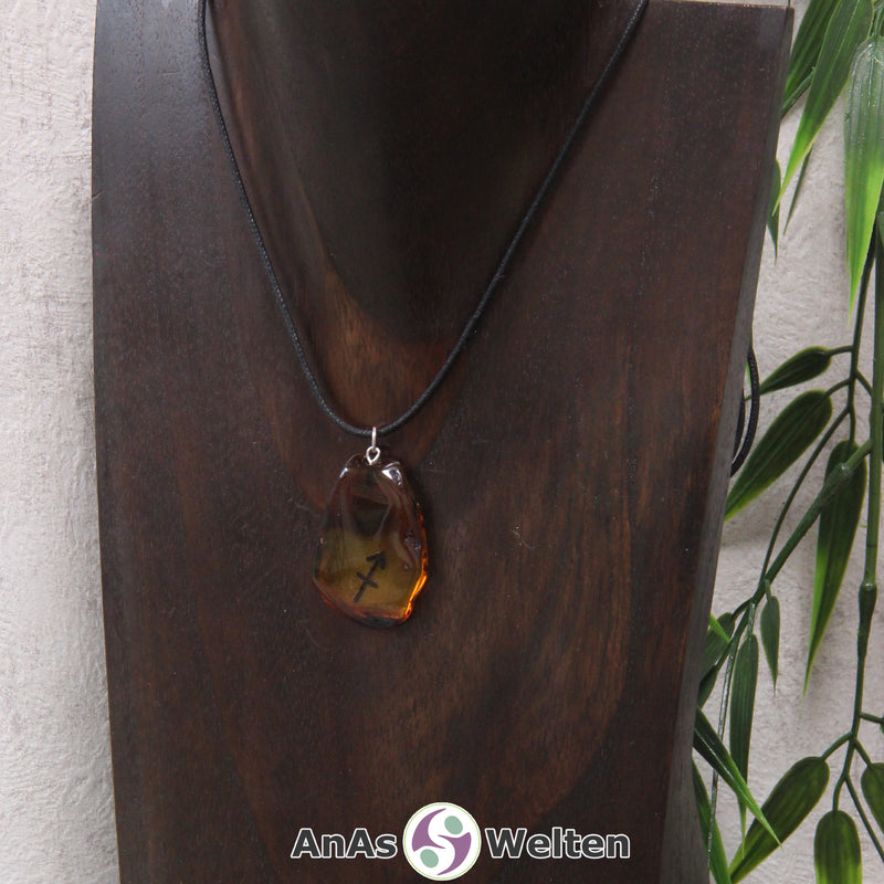 Ein Bernstein Anhänger Schütze an einem Baumwollband als Kette um eine dunkle Büste.