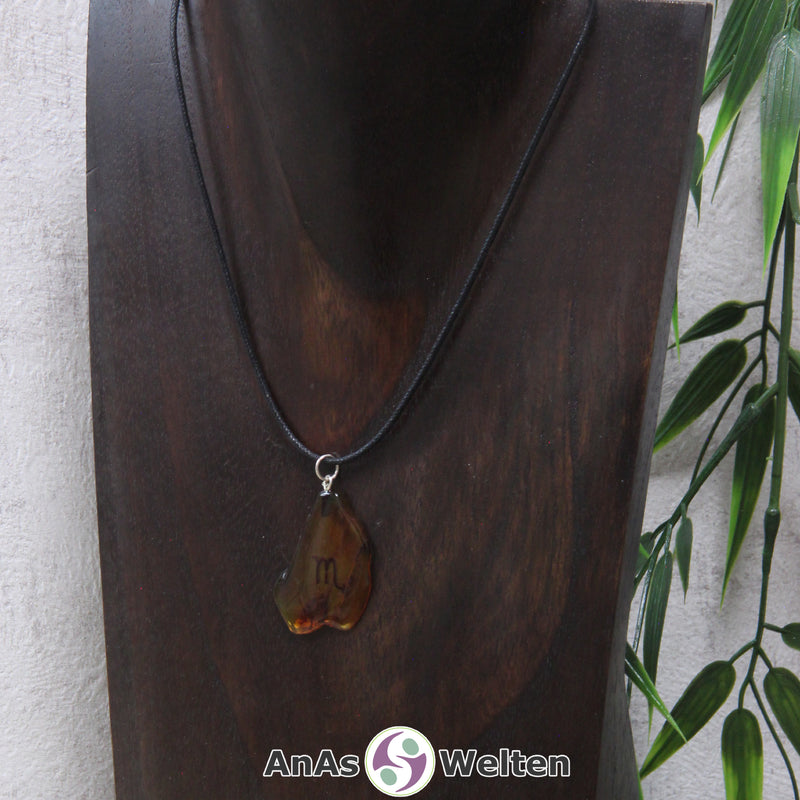 Ein Bernstein Anhänger Skorpion an einem Baumwollband als Kette um eine dunkle Büste.