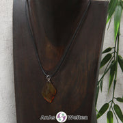 Ein Bernstein Anhänger Steinbock an einem Baumwollband als Kette um eine dunkle Büste.