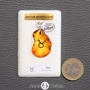 Ein Bernstein Anhänger Stier mit Silberöse an einem Display. Das Sternzeichen ist in den Bernstein eingebrannt.