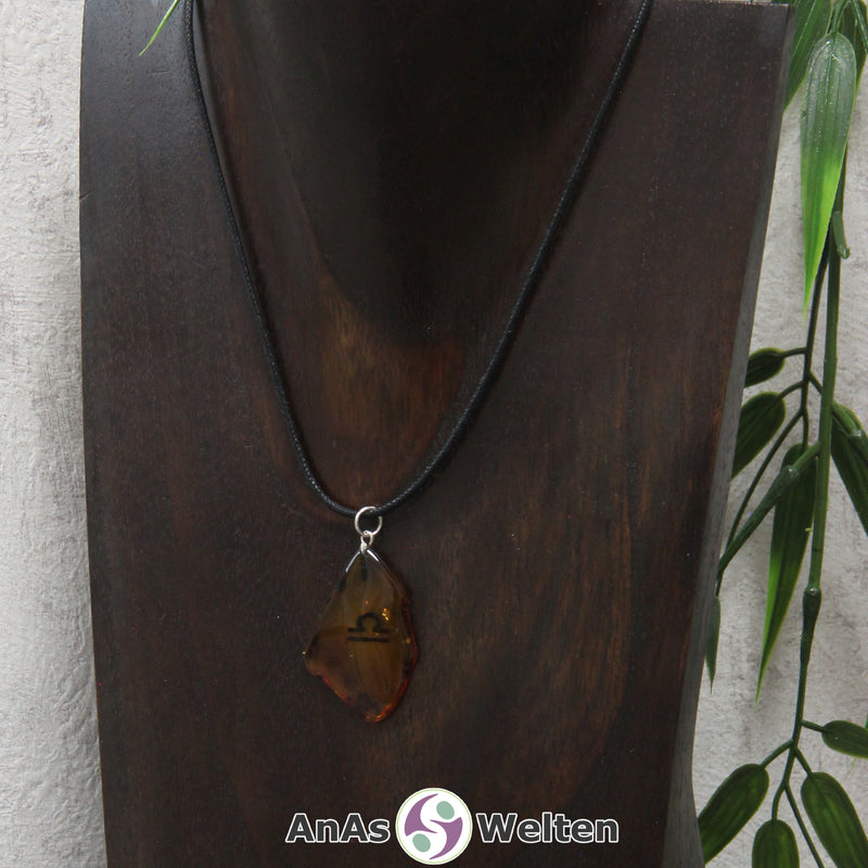 Ein Bernstein Anhänger Waage an einem Baumwollband als Kette um eine dunkle Büste.