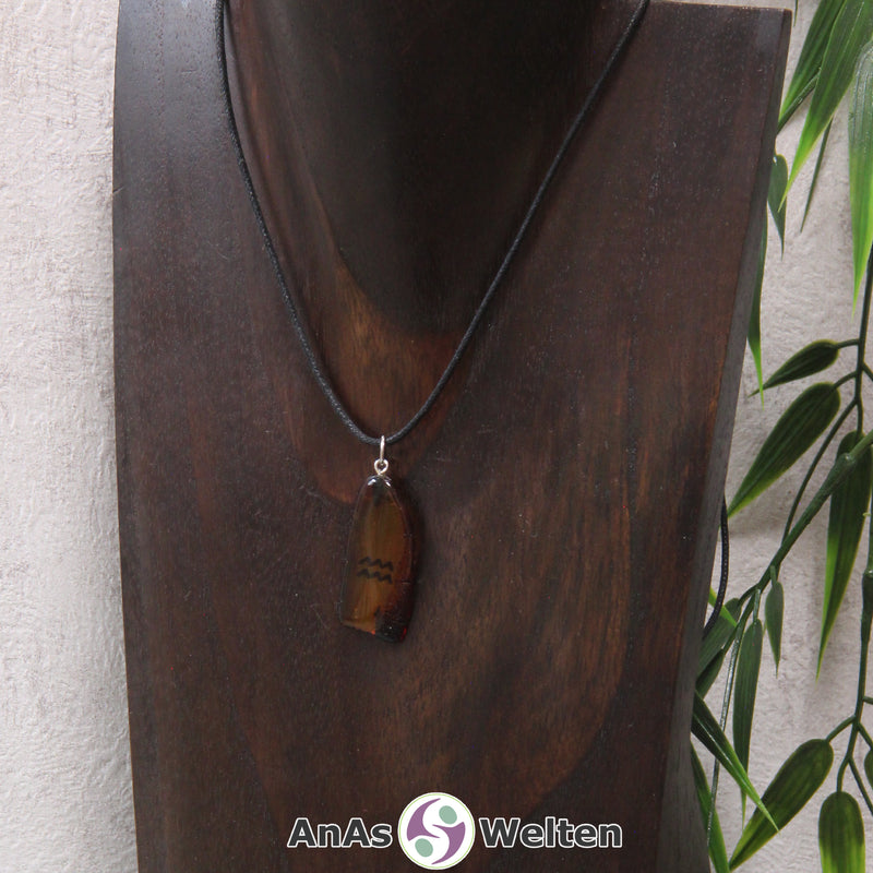 Ein Bernstein Anhänger Wassermann an einem Baumwollband als Kette um eine dunkle Büste.