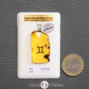 Ein Bernstein Anhänger Zwillinge mit Silberöse an einem Display. Das Sternzeichen ist in den Bernstein eingebrannt.