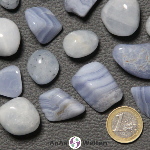 Ein blauer Chalcedon Trommelstein in mehreren Beispielen. Die Edelsteine sind alle hellblau. Einige von ihnen haben deutlich sichtbare Einschlüsse und Risse in ihrem Inneren, während andere in verschiedenen Blautönen gestreift sind.