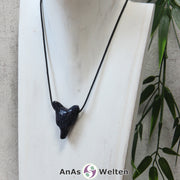 Das Bild zeigt einen Blaufluss Wolf Anhänger an einem Baumwollband. Der Edelstein hat ein tiefes Dunkelblau, das von unzähligen golden glitzernden Punkten durchzogen ist. Das Fellmuster und die Nase sind durch kleine Kerben im Edelstein dargestellt. Die Augen sind kleine schwarze Perlen.