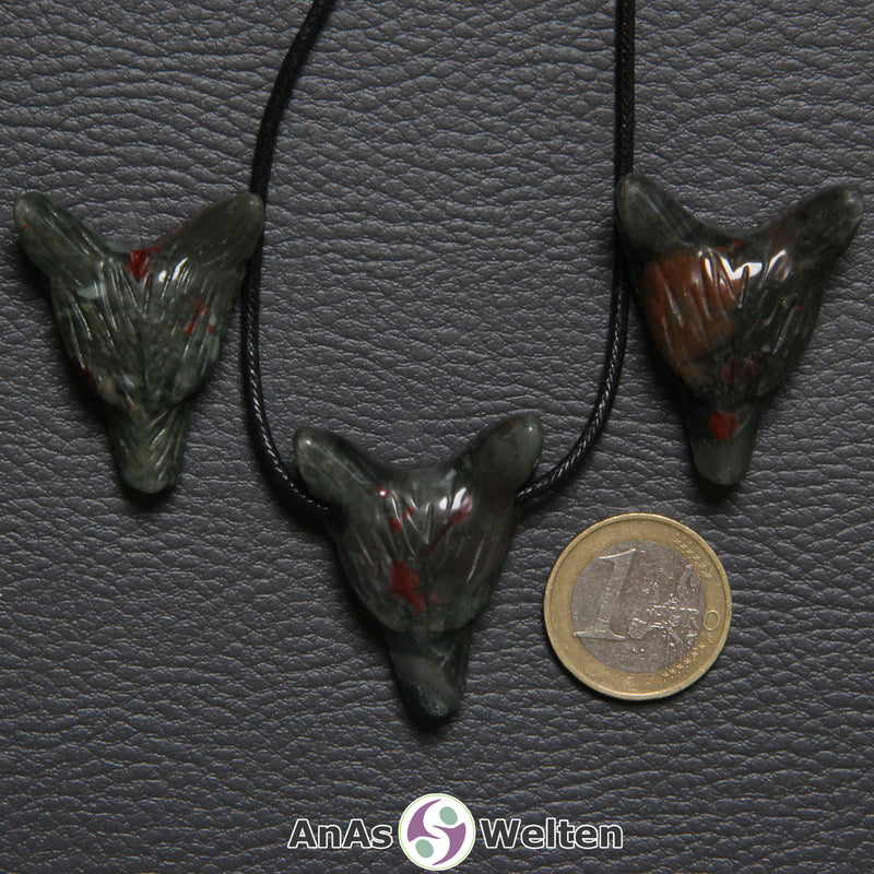 Drei Heliotrop Wolf Anhänger nebeneinander. Einer befindet sich an einem schwarzen Baumwollband.