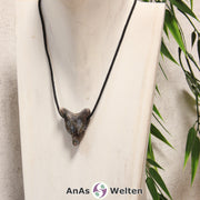 Das Bild zeigt einen Blue Liberty Wolf Anhänger an einem Baumwollband. Der Edelstein hat eine Mischung aus Beige, Braun, Grau und Grau-Blau, die unregelmäßig über den Wolfskopf verteilt ist. Das Fellmuster und die Nase sind durch kleine Kerben im Edelstein dargestellt. Die Augen sind kleine schwarze Perlen.