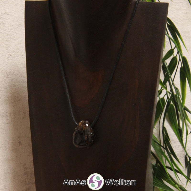 Ein dunkelbrauner Dravit gebohrter Trommelstein an einem schwarzen Baumwollband, der um eine dunkle Büste gehängt wurde.