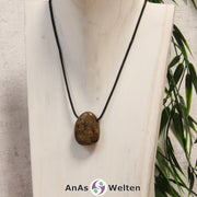 Ein braun-goldener Bronzit gebohrter Trommelstein an einem schwarzen Baumwollband, der um eine helle Büste gehängt wurde.