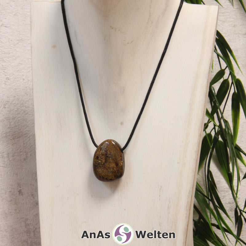 Ein braun-goldener Bronzit gebohrter Trommelstein an einem schwarzen Baumwollband, der um eine helle Büste gehängt wurde.