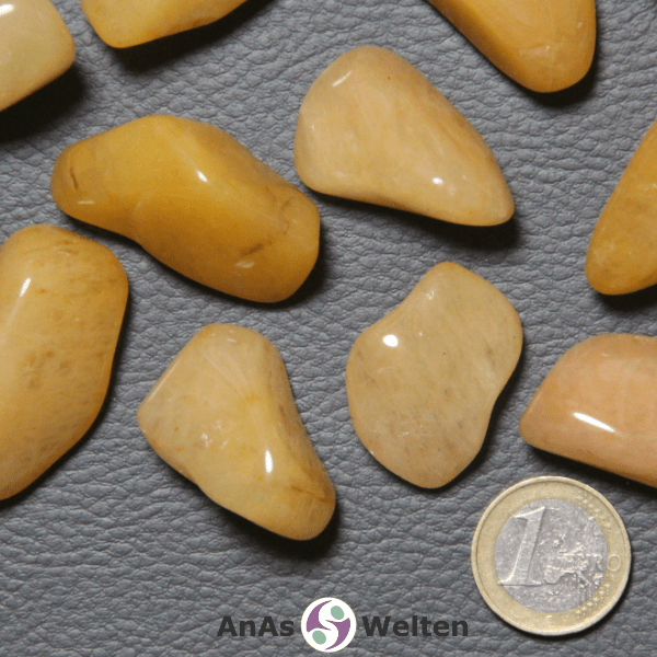 Das Bild zeigt einen Chalcedon Gelb Trommelstein als mehrere Beispiele. Die Steine haben einen warmen Gelbton und eine dezente Musterung, die sich farblich kaum davon unterscheidet. An einigen Stellen sieht man bei einigen Steinen kleine dunkelgelbe bis braune Einschlüsse.