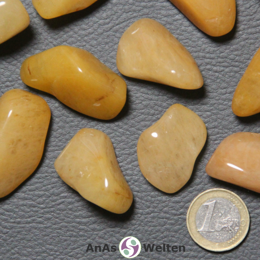 Das Bild zeigt einen Chalcedon Gelb Trommelstein als mehrere Beispiele. Die Steine haben einen warmen Gelbton und eine dezente Musterung, die sich farblich kaum davon unterscheidet. An einigen Stellen sieht man bei einigen Steinen kleine dunkelgelbe bis braune Einschlüsse.