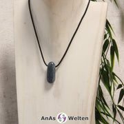 Ein blauer Disthen gebohrter Trommelstein an einem schwarzen Baumwollband, der um eine helle Büste gehängt wurde.