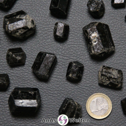 Ein brauner Turmalin Dravit Kristall in mehreren Beispielen. Die Kristalle haben ihre natürlichen glatten und kantigen Seiten. Sie sind schwarz und glänzen in einem leichten Braun.