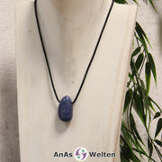 Ein blauer Dumortierit gebohrter Trommelstein an einem schwarzen Baumwollband, der um eine helle Büste gehängt wurde.