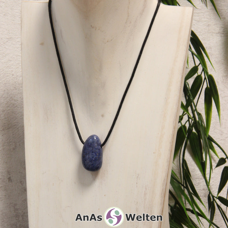 Ein blauer Dumortierit gebohrter Trommelstein an einem schwarzen Baumwollband, der um eine helle Büste gehängt wurde.