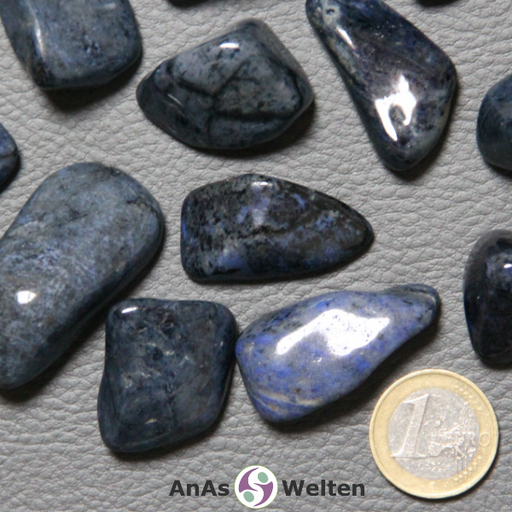 Das Produktbild zeigt einen Dumortierit Trommelstein in mehreren Beispielen. Die Edelsteine haben allesamt eine dunkelblaue Grundfarbe. Einige von ihnen haben hellgraue Einschlüsse, andere schwarze und wieder andere hellblaue.