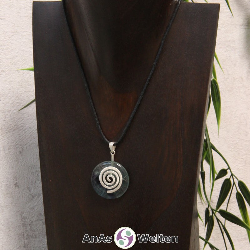 Ein Fluorit Donut an einem Donut-Halter Spirale, der mit einem gewachsten Baumwollband um eine dunkle Büste hängt.