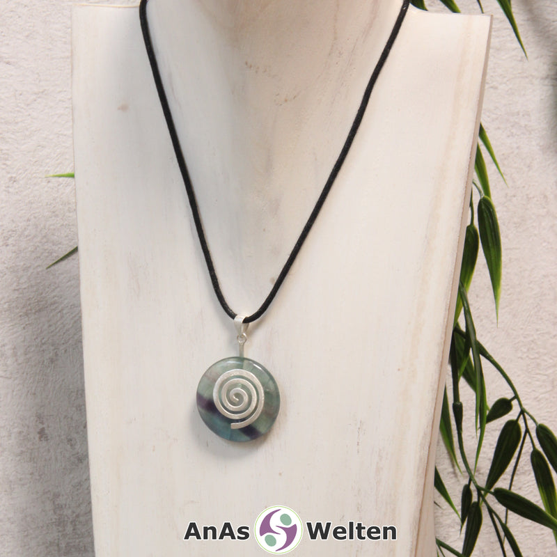 Ein Fluorit Donut an einem Donut-Halter Spirale, der mit einem gewachsten Baumwollband um eine helle Büste hängt.