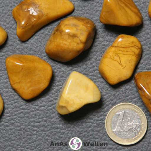 Ein gelber Jaspis Trommelstein wird in mehreren Beispielen dargestellt. Die Edelsteine haben allesamt eine gelb-braune Färbung. Sie sind undurchsichtig und viele von ihnen von dunkelbraunen Musterungen durchzogen.