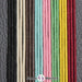 Das Bild zeigt ein gewachstes Baumwollband anhand dreier Beispiele in den jeweiligen Farben. Von links nach rechts sind das die Farben schwarz, beige, braun, türkis, rosa, grün, gelb und rot.