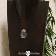 Ein gebohrter Girasol Trommelstein an einem Baumwollband. Der Edelstein hat eine schwach milchige, fast vollkommen durchsichtige Farbe.