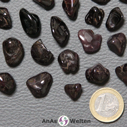 Das Bild zeigt den Granat Trommelstein als mehrere Beispielsteine. Die Edelsteine sind dunkelrot bis schwarz und haben gelegentliche hellere Stelle. Sie sind zwar geschliffen, haben aber trotzdem eine unebene Form.