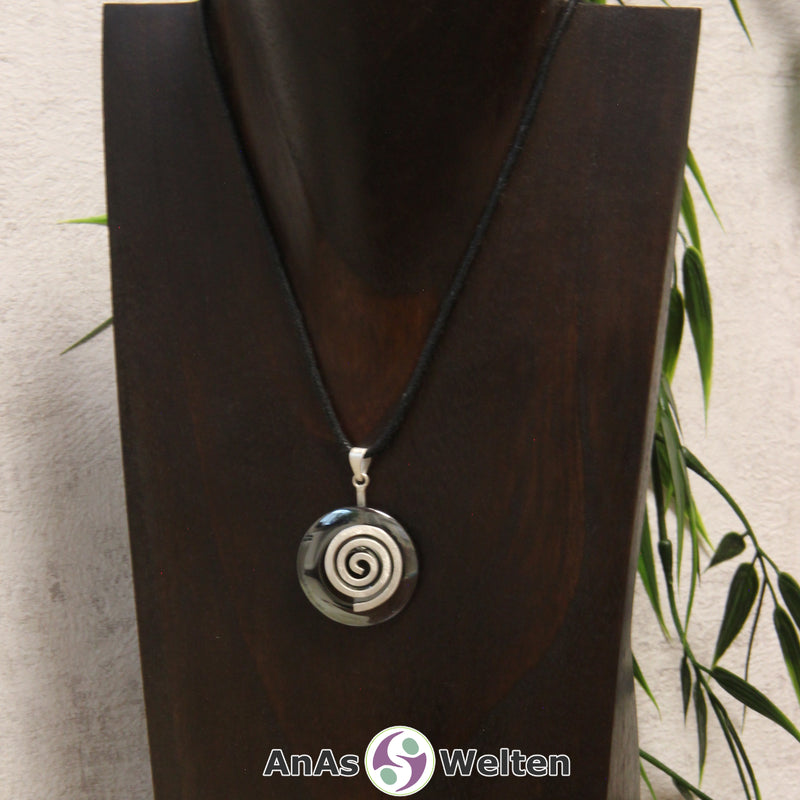 Ein Hämatit Donut an einem Donut-Halter Spirale, der mit einem gewachsten Baumwollband um eine dunkle Büste hängt.