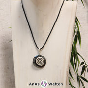 Ein Hämatit Donut an einem Donut-Halter Spirale, der mit einem gewachsten Baumwollband um eine helle Büste hängt.