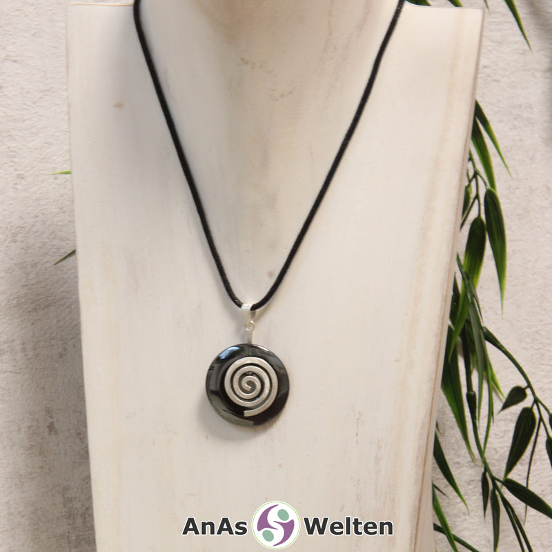 Ein Hämatit Donut an einem Donut-Halter Spirale, der mit einem gewachsten Baumwollband um eine helle Büste hängt.