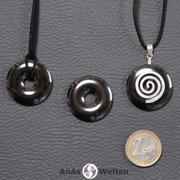 Drei Hämatit Donuts nebeneinander. Einer an einem Baumwollband, ein anderer an einem Donut-Halter mit Baumwollband.