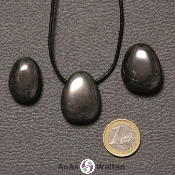 Drei silbergraue Hämatit gebohrte Trommelsteine nebeneinander. Einer befindet sich an einem schwarzen gewachsten Baumwollband.